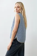 Chaleco capitoneado reversible a rayas azules y blancas con ribete color crema. Tiene cuello redondo, cierre con botones a presión y bolsillos de parche. El reverso es liso color tostado.