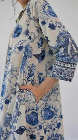 Vestido camisero de manga larga, color blanco con estampado azul de motivos marinos como medusas, conchas y corales. Tiene cuello camisero y bolsillos laterales.
