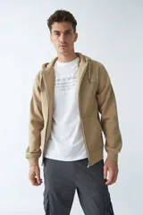 Campera de felpa color beige con cierre frontal, capucha con cordón ajustable, bolsillos laterales y logo estampado en el pecho.