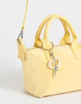 Cartera amarilla con doble asa corta de mano y correa regulable desmontable. Incluye charm colgante de perlas y cierre superior.