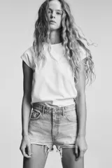 Short de jean de tiro alto, color celeste claro desgastado, con roturas grandes y deshilachado en el bajo. Presenta cinco bolsillos y cierre frontal con botón metálico.