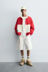 Bermuda de denim color blanco roto con efecto encerado, corte amplio (baggy fit) y cinco bolsillos. Presenta cierre frontal con cremallera y botón.