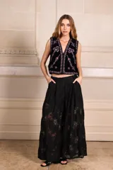 Chaleco color beige con bordados florales en tonos violeta y rosa, sin mangas y con cierre frontal con ganchos.