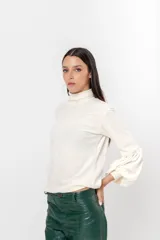 Polera de plush color blanco con cuello alto y mangas largas abullonadas.
