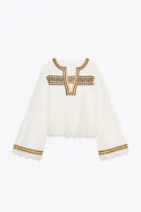 Camisa blanca de algodón y lino, con cuello redondo y escote pico. Tiene mangas largas acampanadas y bordados a contraste con puntilla.