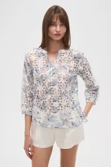 Blusa blanca de algodón con bordado broderie inglés y estampado floral en tonos azules y marrones. Posee cuello en V con abertura y botones frontales, y mangas tres cuartos.