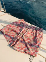 Short de baño para hombre con estampado de hojas en tonos rojo, verde y celeste. Tiene elástico en la cintura, cordón ajustable, tres bolsillos y mesh interior hipoalergénico.