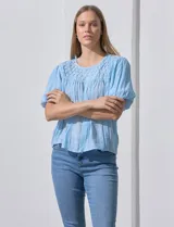 Blusa celeste con escote redondo y mangas cortas abullonadas. Presenta detalle de frunces en el canesú.