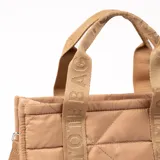 Bolso tipo shopper color beige con diseño acolchado en forma de rombos. Tiene doble asa corta con la inscripción "TOTE BAG" y correa larga extraíble. Cierre superior con cremallera y bolsillo interno.