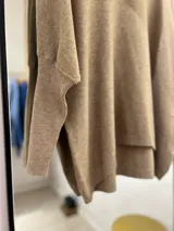 Polerón color camel de corte oversize, con cuello drapeado y mangas largas caídas. La parte delantera es más corta que la trasera.