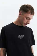 Remera negra de manga corta con cuello redondo y estampado frontal con el logo de la marca "Mistral" y la leyenda "Creative goods for living, working & playing since 1976".