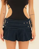 Minifalda plisada de mezclilla oscura con costuras blancas contrastantes. Presenta un cinturón incorporado con dos hebillas metálicas grandes y ajustables.