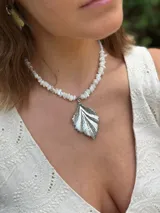 Gargantilla de cuentas de piedra color crema con dije colgante dorado en forma de hoja.