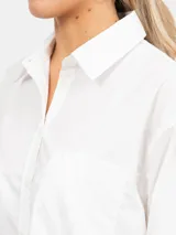 Vestido camisero corto, color azul, con cuello solapa, manga larga y bolsillo delantero de plastrón. Presenta un bajo asimétrico.