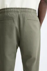 Pantalón de jogging color beige confeccionado en tejido de mezcla de algodón. Cuenta con cintura elástica ajustable con cordón, bolsillos frontales y traseros.