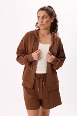 Conjunto deportivo color marrón, compuesto por un buzo con capucha, cierre frontal, bolsillos y terminaciones metálicas, y un short con cintura elástica ajustable con cordón.