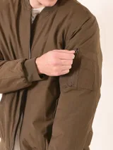 Chaqueta tipo bomber color verde militar, con cierre frontal, cuello y puños acanalados. Presenta bolsillo utilitario con cierre en la manga izquierda y bolsillos frontales con solapa y broche.