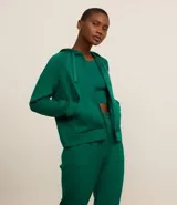 Campera deportiva verde esmeralda de modal, con capucha ajustable con cordón, cierre frontal con cremallera y bolsillos laterales.
