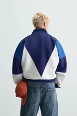 Chaqueta deportiva azul marino, azul y blanca con cuello alto, cierre frontal con cremallera, bolsillos laterales y puños y bajo acanalados.