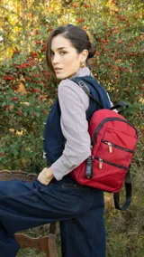 Mochila roja de tafeta con cierre superior y tiradores metálicos. Incluye bolsillos internos, bolsillo frontal con doble cierre metálico, asas rígidas y correas regulables para colgar en la espalda.