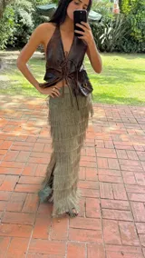 Falda larga color verde oliva con múltiples capas de flecos largos, creando un efecto texturizado. La falda tiene un tajo lateral.