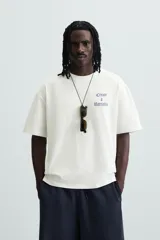Camiseta blanca de corte holgado con cuello redondo y mangas cortas. Estampa en el pecho con la frase "Create a Narrative" en azul.