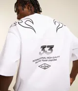 Remera blanca de corte oversized, confeccionada en tejido de malla de algodón. Presenta cuello redondo, mangas cortas y estampados con lettering y motivos maoríes en color negro.