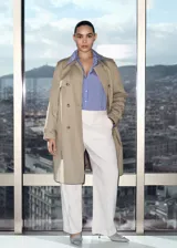 Trench coat azul marino con doble botonadura, cinturón ajustable, cuello de solapa, trabillas en los puños y abertura posterior en el bajo.