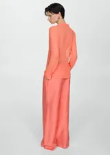 Blusa color salmón de tejido fluido semitransparente, con cuello camisero, manga larga con puños abotonados y cierre frontal con botones.