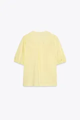 Camisa color amarillo claro de popelín con lyocell, cuello redondo con escote pico, manga corta con elástico y cierre frontal con lazadas.