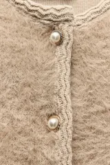 Chaqueta color beige de tejido de punto con efecto pelo, cuello redondo, manga larga y cierre frontal con botones tipo perla.