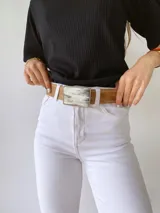 Cinto de cuero color marrón con forro de cuero y hebilla rectangular con diseño de guampa en blanco y negro con marco metálico plateado.