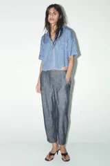 Camisa cropped de viscosa y lino a rayas verticales azules y blancas. Tiene cuello solapa, escote pico, manga corta con vuelta y bolsillos de plastrón.