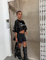 Minifalda negra de jean con tablas, abertura lateral y cinturón con hebilla metálica.