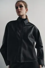 Sobrecamisa negra de efecto piel, con cuello de solapa, manga larga con puños abotonados, bajo recto y cierre frontal con botones.