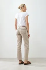 Pantalón de jean color beige, de corte recto, con bolsillos laterales y traseros. Se ajusta a la cintura con cinturón de cuero marrón.