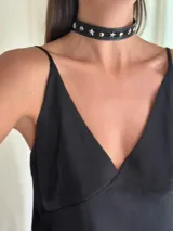Gargantilla tipo choker de cuero sintético negro, con apliques de estrellas y remaches plateados. Se cierra con cadena y mosquetón para ajustar el largo.