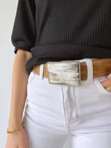 Cinto de cuero color marrón con forro de cuero y hebilla rectangular con diseño de guampa en blanco y negro con marco metálico plateado.