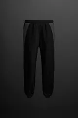 Pantalón de jogging negro con paneles laterales en gris, confeccionado en tejido técnico ligero y elástico. Cuenta con cintura elástica ajustable con cordón interior, bolsillos delanteros y bajo acabado en elástico ajustable con cremallera.