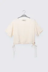 Top color crema de lino y Tencel, con mangas cortas y lazo ajustable en el ruedo.