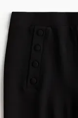 Pantalón negro de punto grueso, tiro alto con elástico oculto, botones decorativos adelante y piernas rectas de corte holgado.