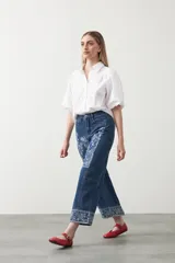 Pantalón de denim azul oscuro con bordado estilo bandana en blanco en los laterales de las piernas y en los puños. El corte es recto y amplio, llegando al tobillo.