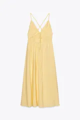 Vestido midi amarillo de tejido fluido con escote pico y tirantes finos cruzados en la espalda ajustables con lazada. Tiene detalle de elásticos bajo el pecho.