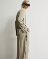 Blazer recto color topo (beige grisáceo) de viscosa, con solapa y cierre de dos botones. Presenta un diseño artístico con trazos oscuros simulando pintura en la solapa, costuras de la manga y un bolsillo de vivo con solapa en el lado derecho, mientras que el bolsillo izquierdo es pintado.