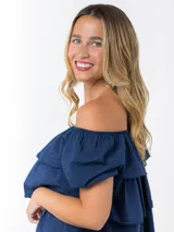 Blusa azul marino de algodón italiano, con escote elastizado que permite usarla con los hombros al descubierto o como remera con hombro abullonado. Presenta volados y mangas cortas abullonadas.