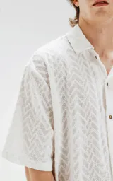 Camisa blanca de manga corta con textura calada y cierre con botones marrones.