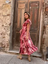 Vestido largo de seda con estampado tie-dye en tonos rojo y blanco, con mangas cortas con volados y ruedo con volados.