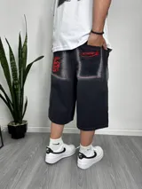 Bermuda de jean negro con corte ancho y largo a la rodilla. Tiene bolsillos traseros con bordados rojos de llamas y la palabra "Street".