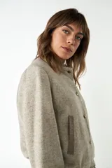 Campera estilo bomber de cuello redondo, color beige jaspeado, con cierre frontal de broches y bolsillos delanteros con ribete marrón.
