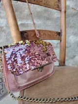 Cartera bandolera rectangular con solapa, cubierta de lentejuelas rosas y doradas. Incluye correa de cuero sintético rosa con tachas y correa de cadena dorada.